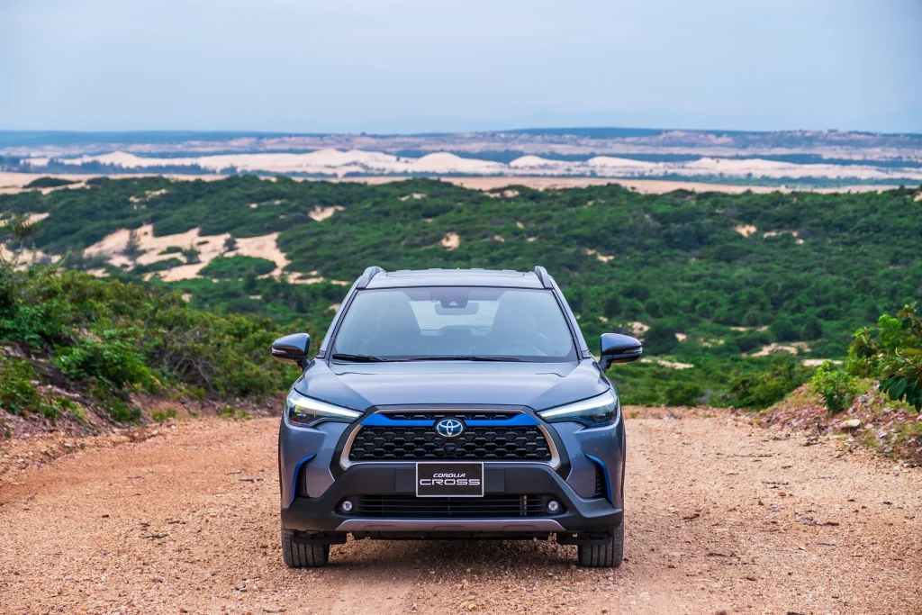 đầu xe Toyota Corolla Cross 2024 màu xanh xám đi trên đường đất cát